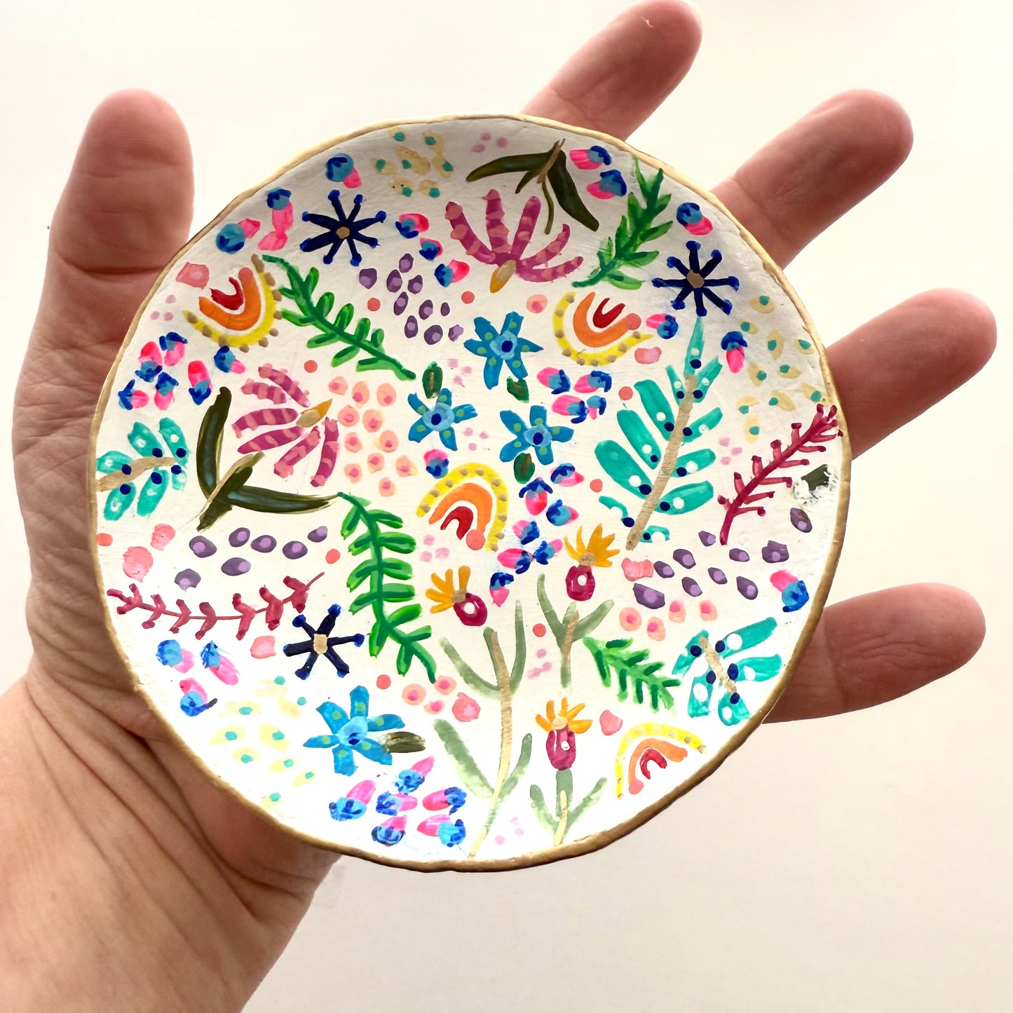 In my Hand I’m holding a small handmade clay plate with colorful floral patterns by Phoenix artist Julie Hamilton