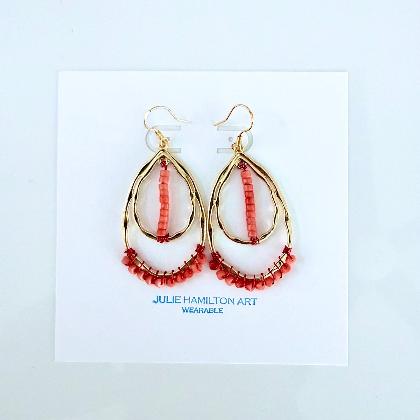 Gold teardrop earrings with coral beads on a white card, featuring 'Julie Hamilton Art - wearable'.