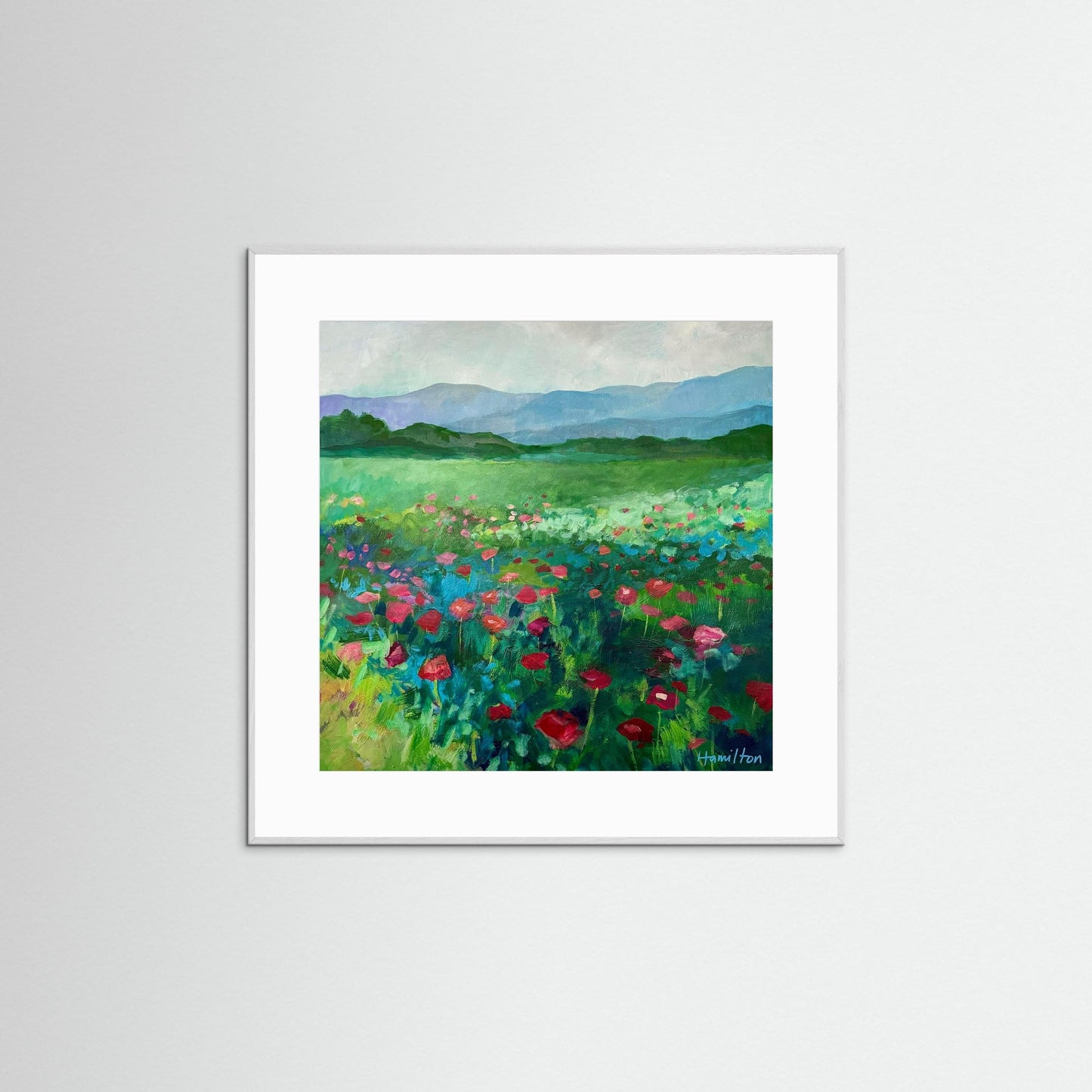 white Framed painting of a field with flowers and mountains on a white wall