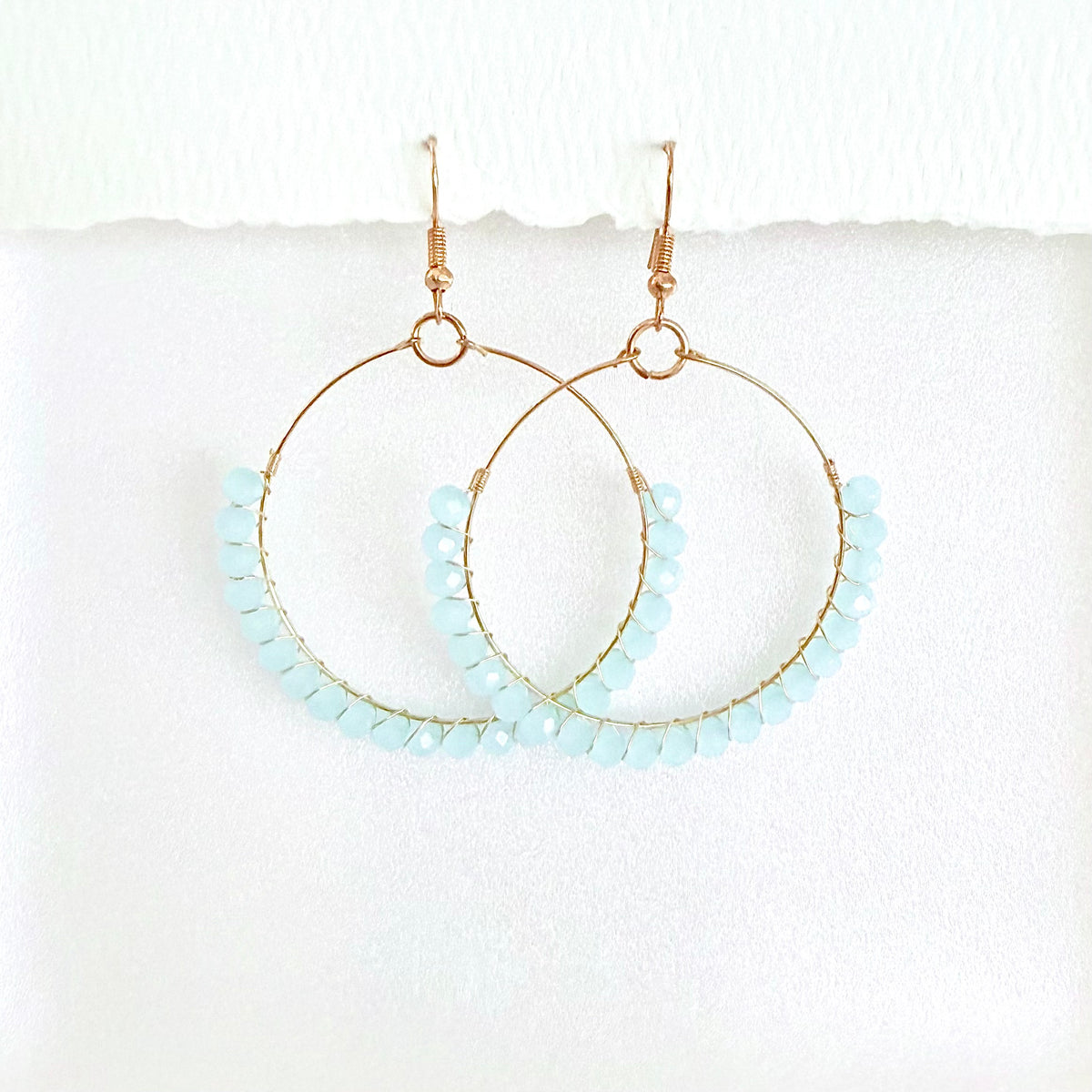 Gold hoop earrings with light blue beads on a white background by Phoenix artist Julie Hamilton 