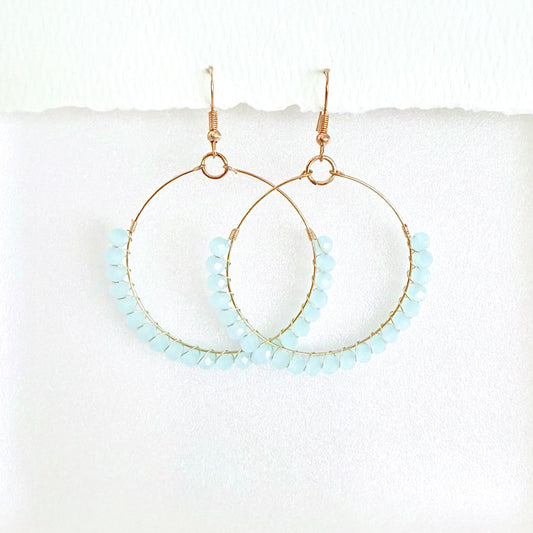 Gold hoop earrings with light blue beads on a white background by Phoenix artist Julie Hamilton 