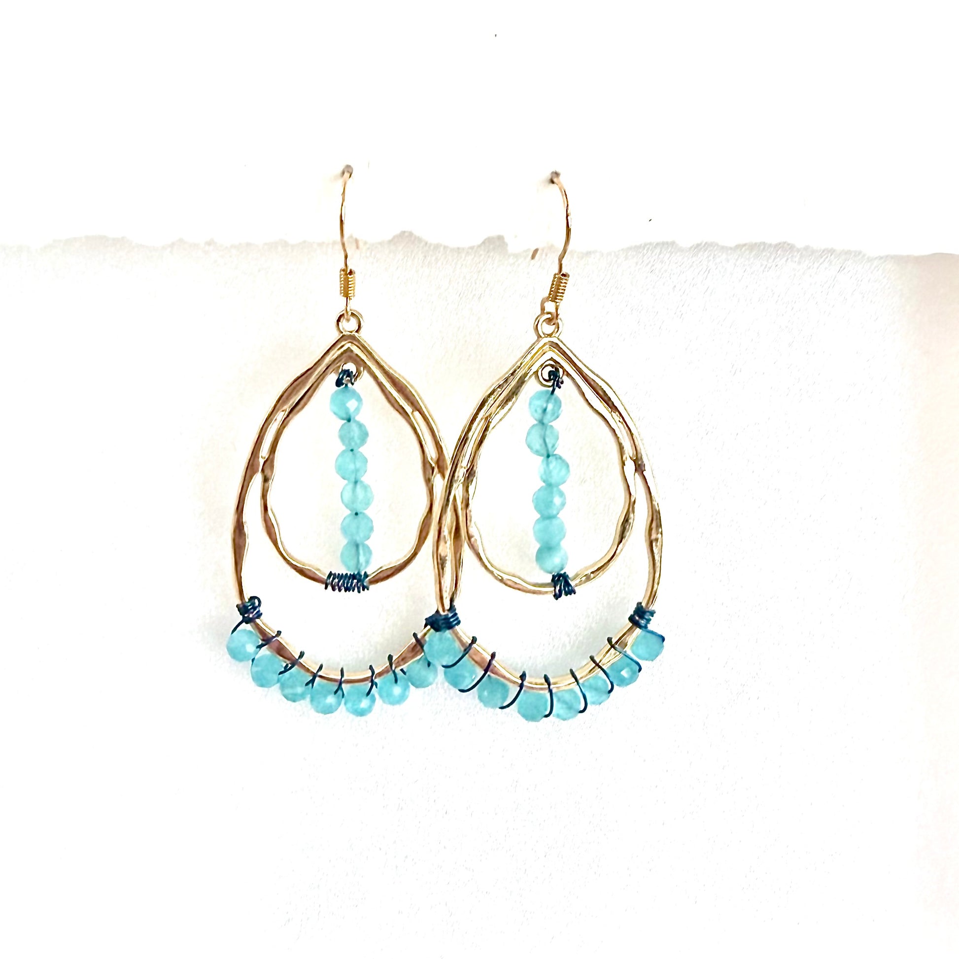 Gold double teardrop earrings with aquamarine blue beads on a white background