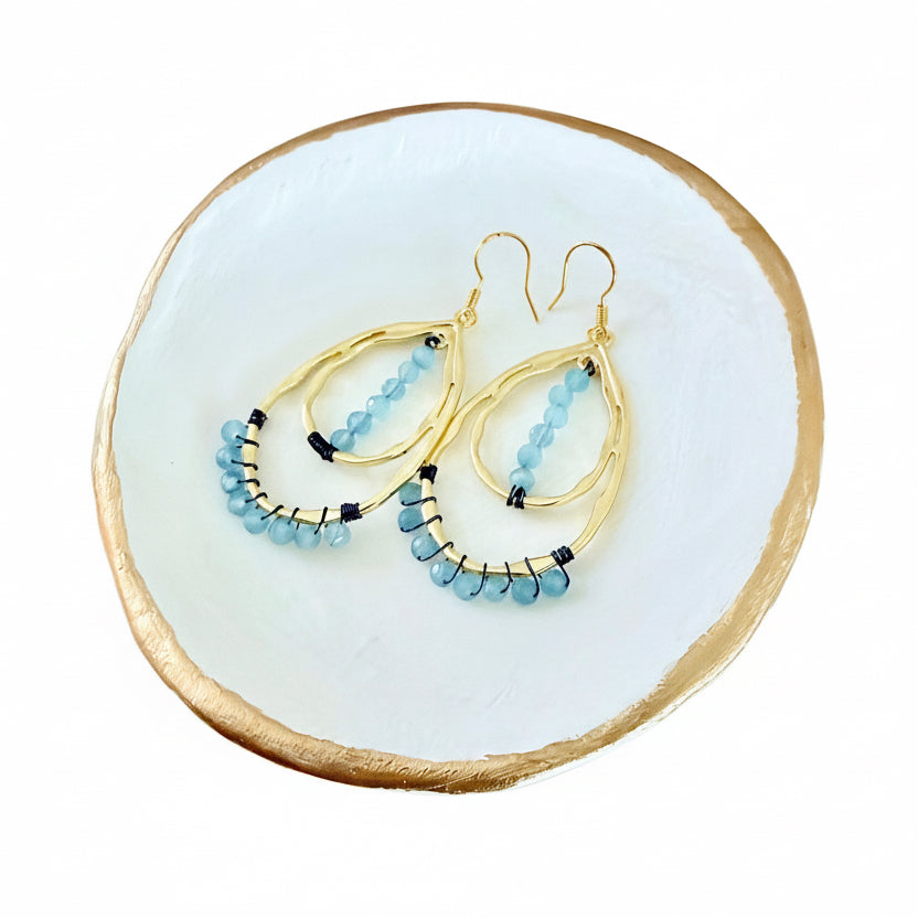 Gold double teardrop earrings with blue aquamarine beads on a gold rimmed dish