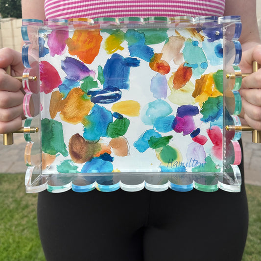 An 8” x 10” clear acrylic tray with colorful watercolor palette print bottom held by gold handles outside of phoenix Az studio