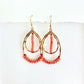 Gold teardrop earrings with coral beads on a white background by Julie Hamilton