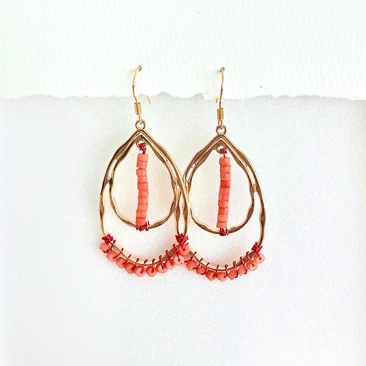 Gold teardrop earrings with coral beads on a white background by Julie Hamilton