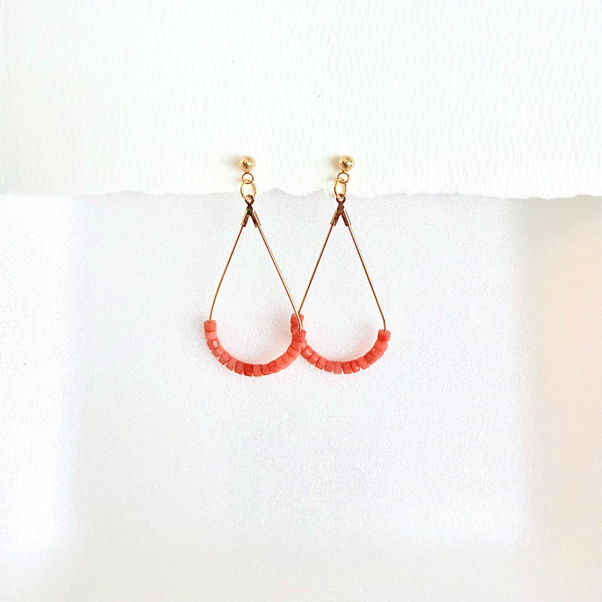 Pair of gold teardrop earrings with coral beads on a white background by artist Julie Hamilton