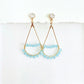 Pair of gold teardrop earrings wrapped with light blue aquamarine beads on a white background by artist Julie Hamilton