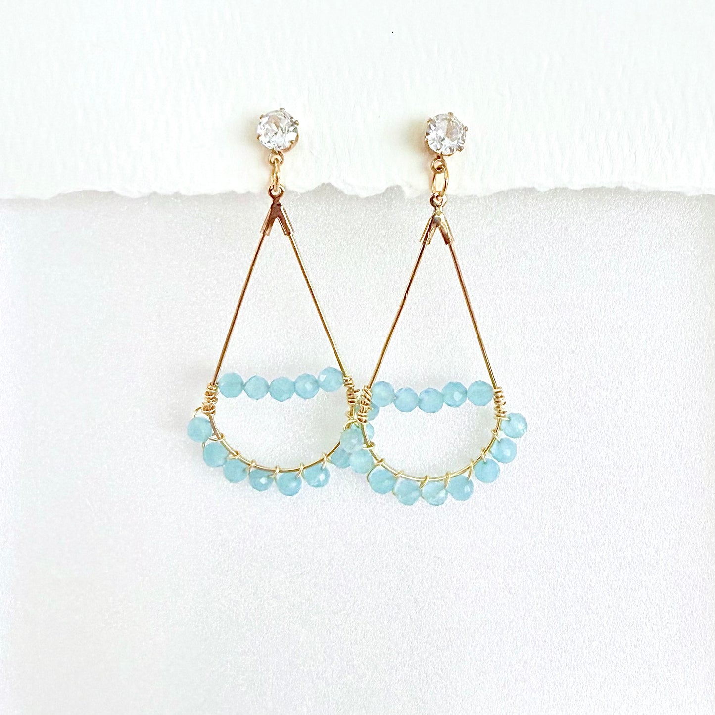 Pair of gold teardrop earrings wrapped with light blue aquamarine beads on a white background by artist Julie Hamilton