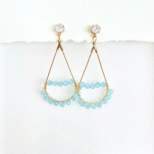 Pair of gold teardrop earrings wrapped with light blue aquamarine beads on a white background by artist Julie Hamilton