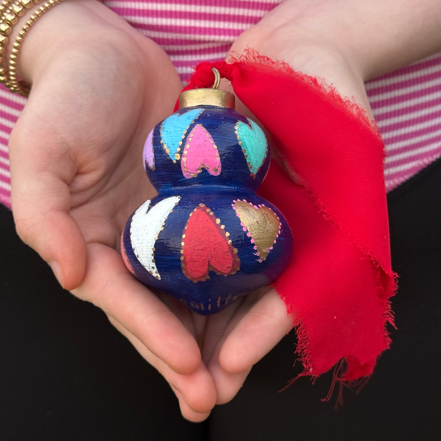 Decorative ceramic Christmas ornament with heart patterns held by hands against a black background by Phoenix artist Julie Hamilton
