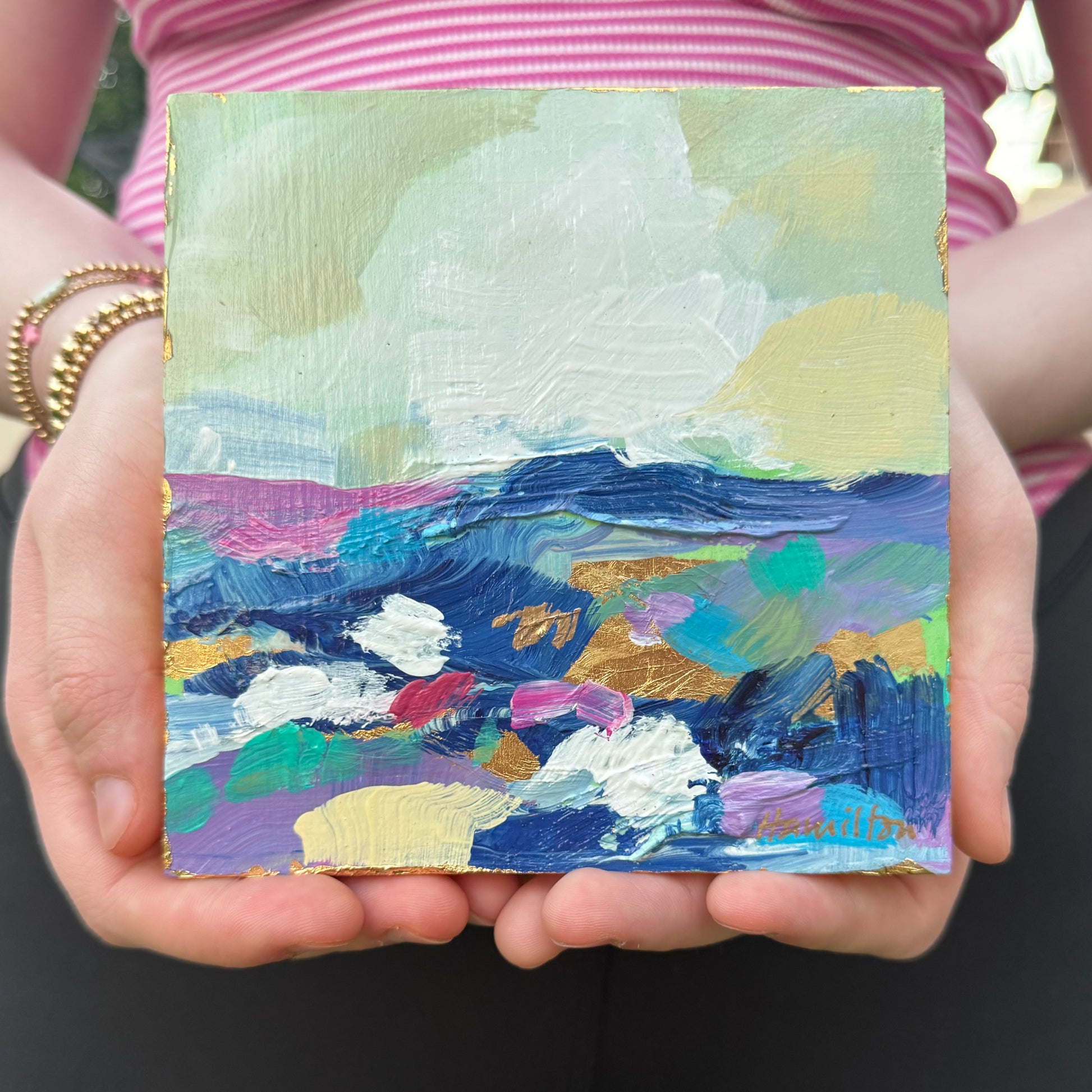 Two hands holding a small abstract landscape painting with colorful brushstrokes by Phoenix artist Julie Hamilton