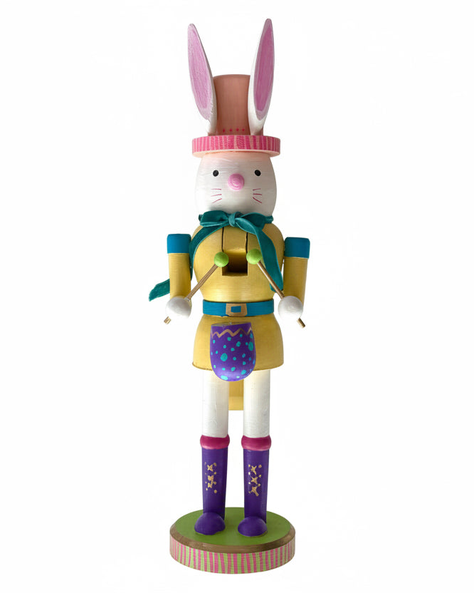 Hand painted Easter nutcracker figure of a rabbit in a yellow outfit with a pink hat on a white background by professional artist Julie Hamilton