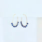 Pair of gold hoop earrings with blue lapis lazuli beads on a white background by artist Julie Hamilton