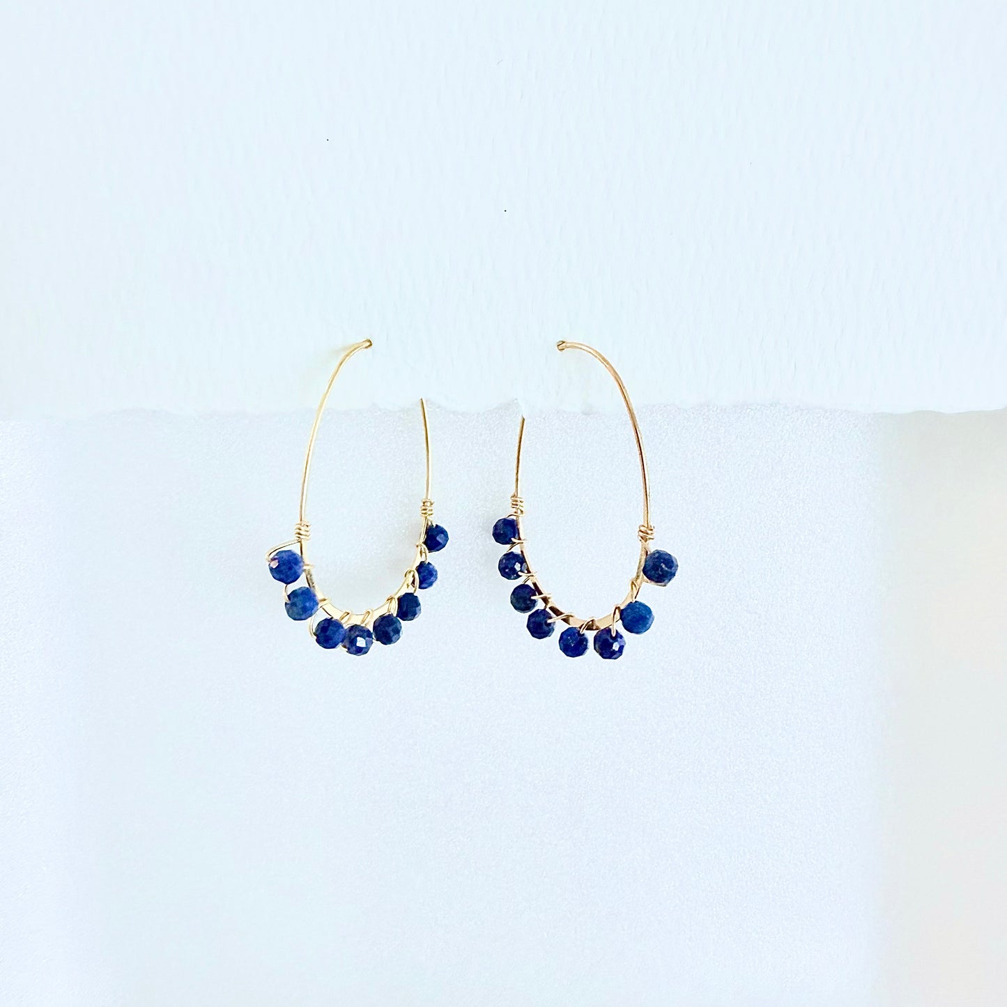 Pair of gold hoop earrings with blue lapis lazuli beads on a white background by artist Julie Hamilton