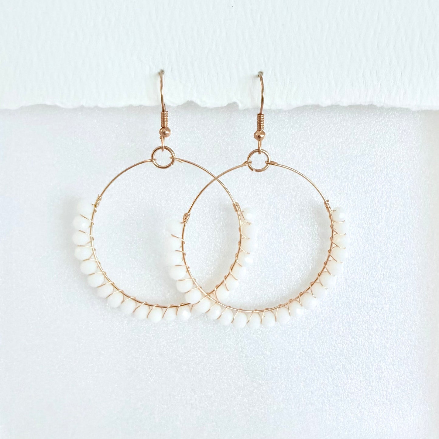 Gold hoop earrings wrapped with white beads on a white background by Phoenix artist Julie Hamilton