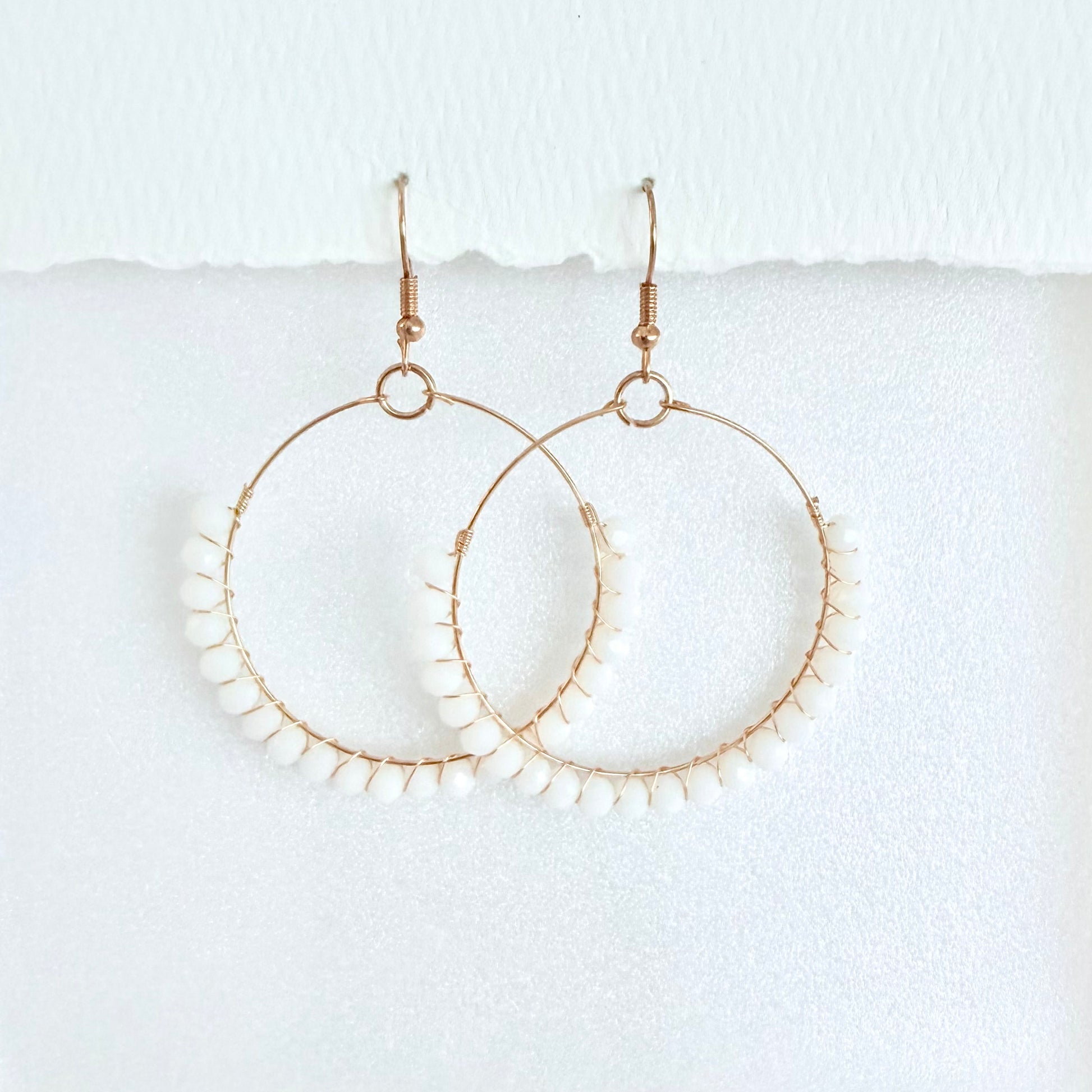 Gold hoop earrings wrapped with white beads on a white background by Phoenix artist Julie Hamilton
