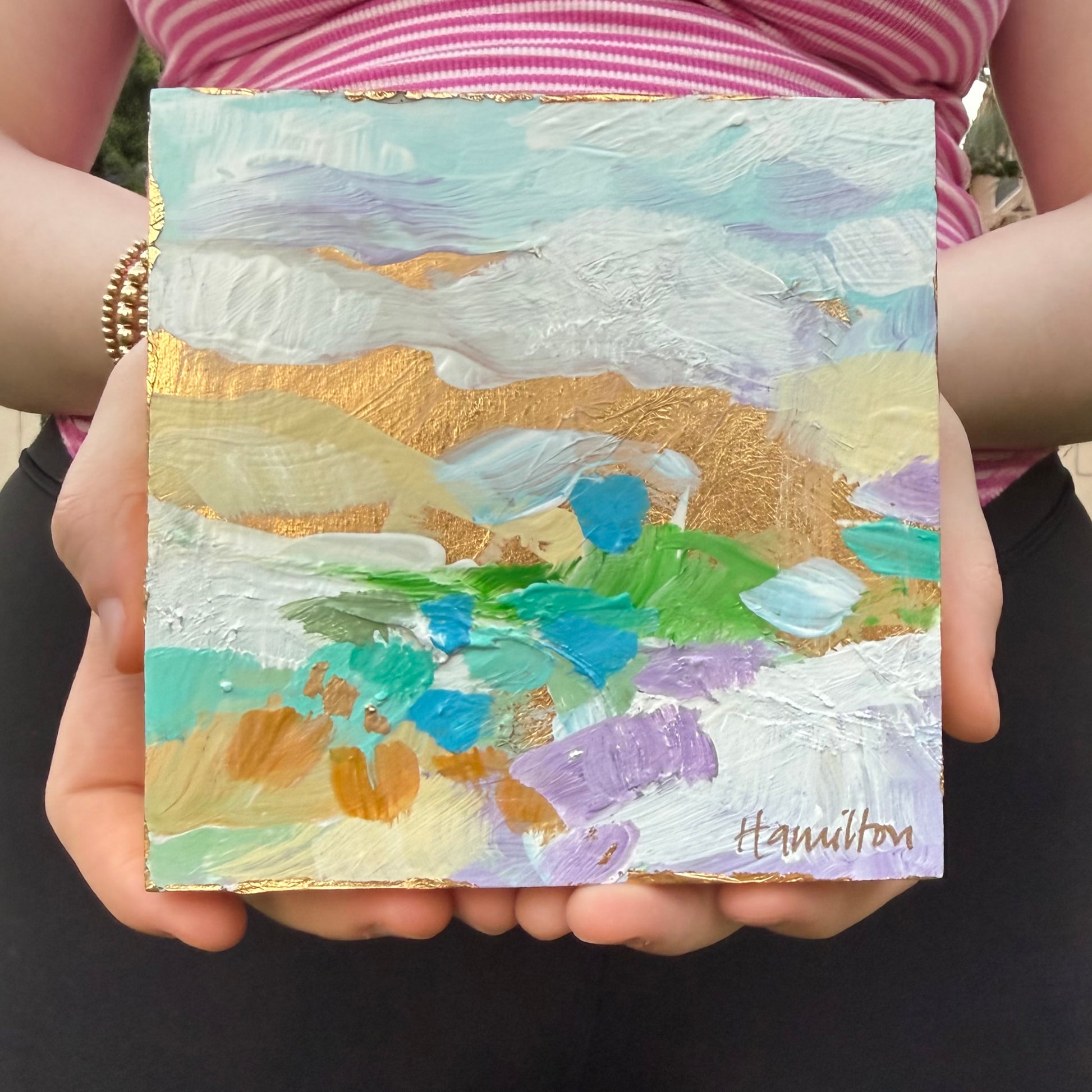 Hands holding a small square colorful abstract landscape painting with gold leaf accents by Phoenix artist Julie Hamilton