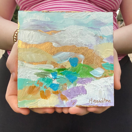 Hands holding a small square colorful abstract landscape painting with gold leaf accents by Phoenix artist Julie Hamilton