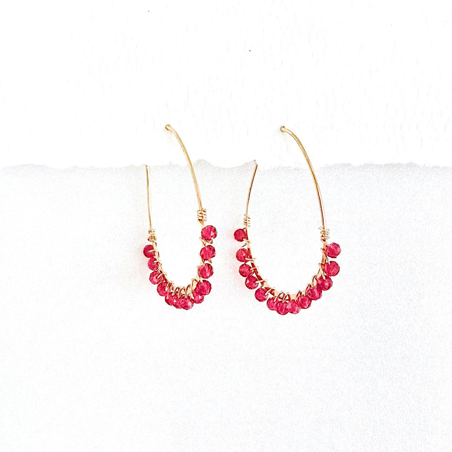 Gold hoop earrings with faceted pink beads on a white background by artist Julie Hamilton