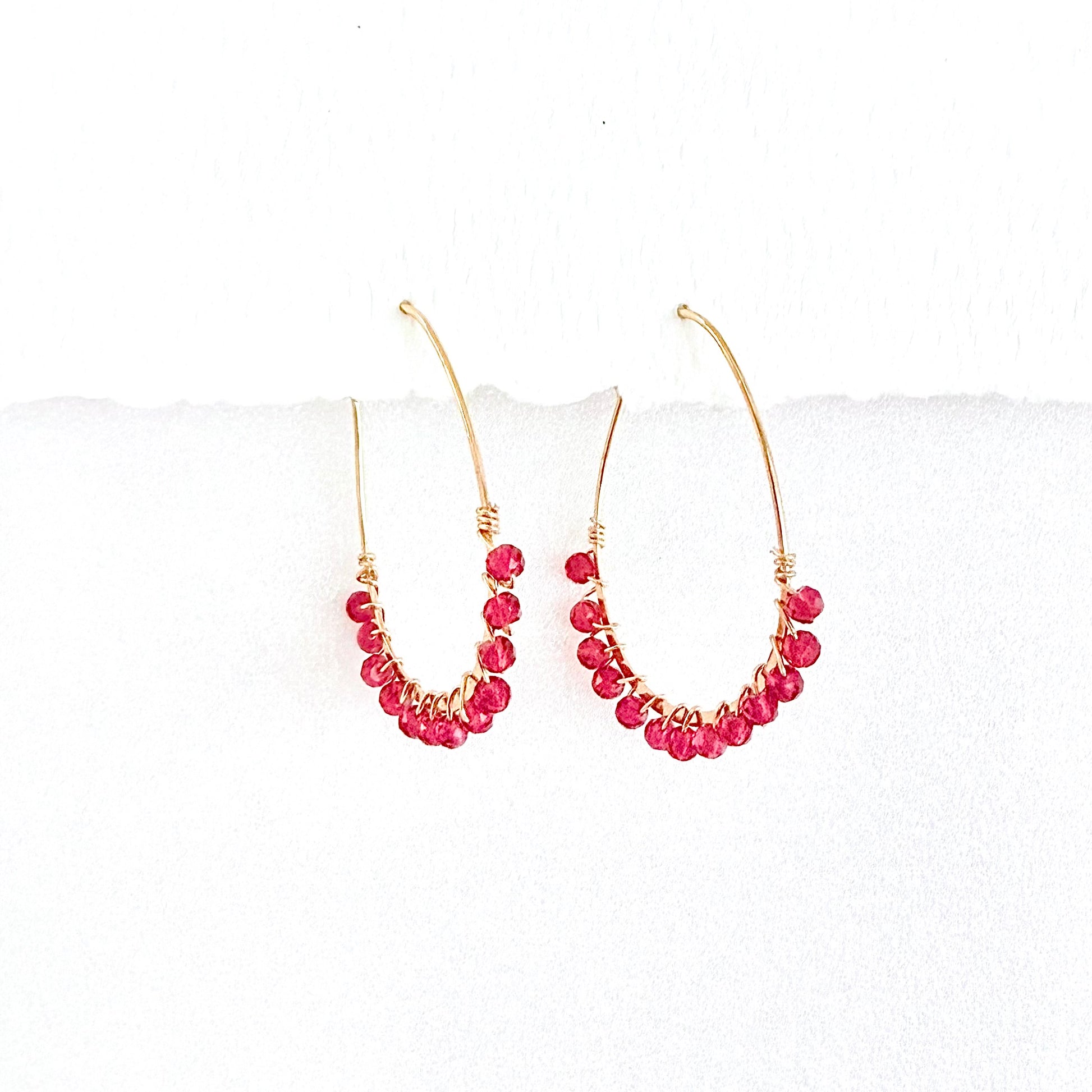 Gold hoop earrings with faceted pink beads on a white background by artist Julie Hamilton