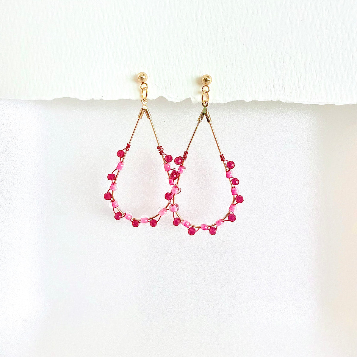 Pair of beaded earrings with pink and red beads on a white background by artist Julie Hamilton