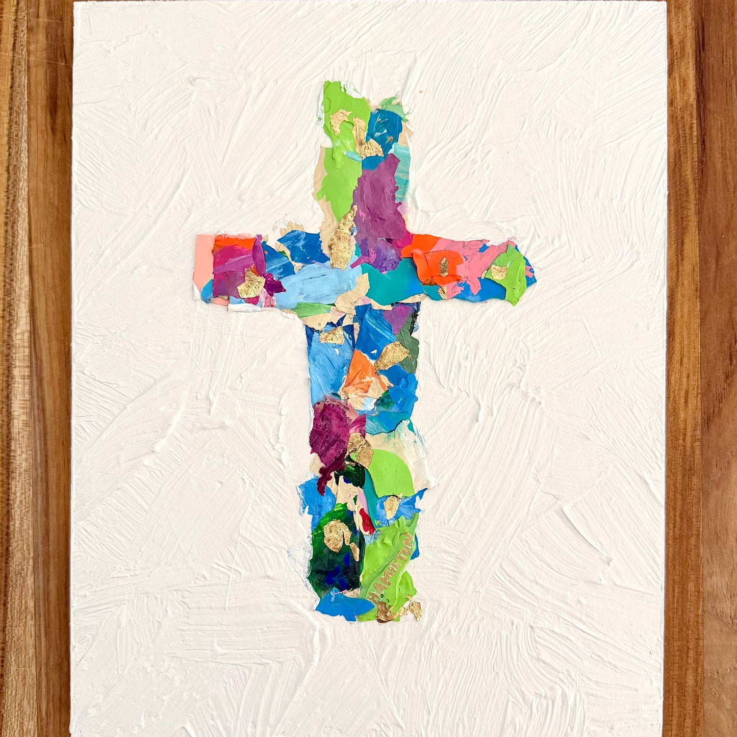 Colorful cross-shaped collage on a textured white canvas with a wooden background