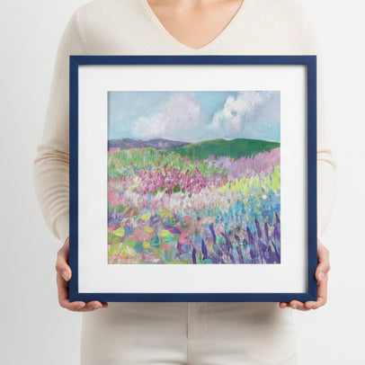 Person holding a framed painting of a colorful landscape