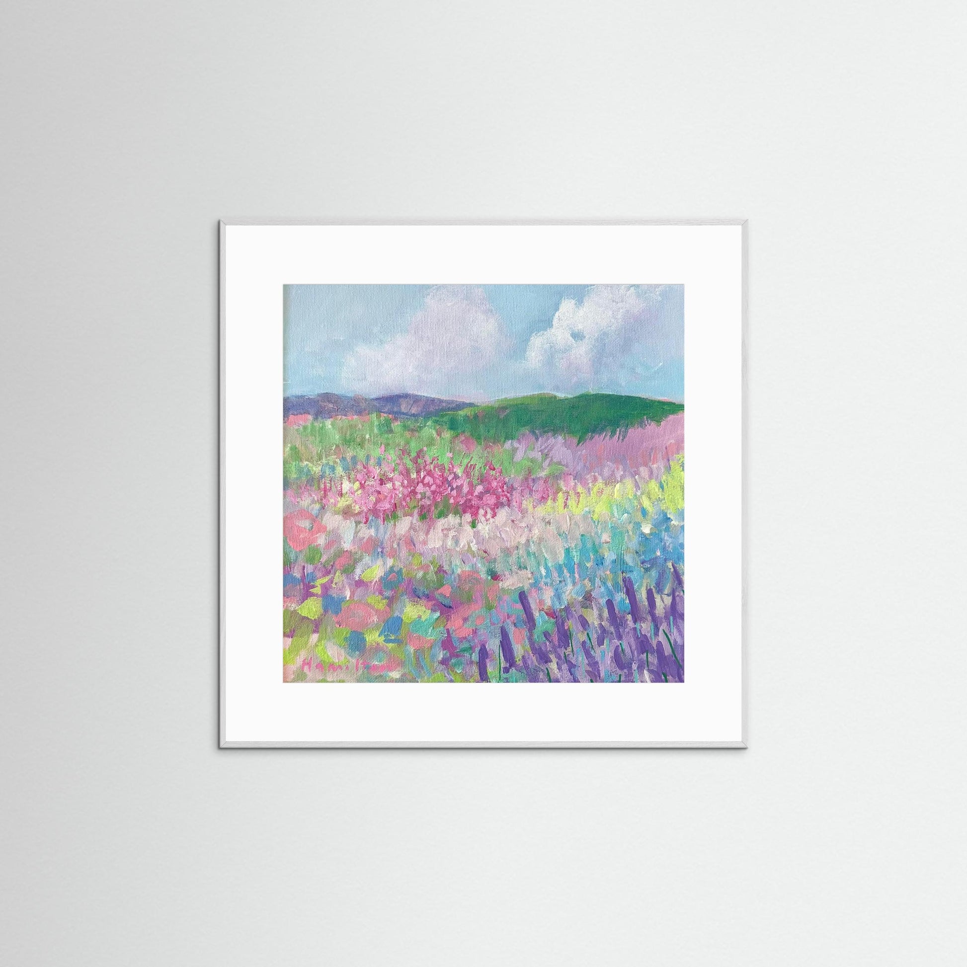 Framed artwork of a colorful landscape with flowers and mountains on a white wall.