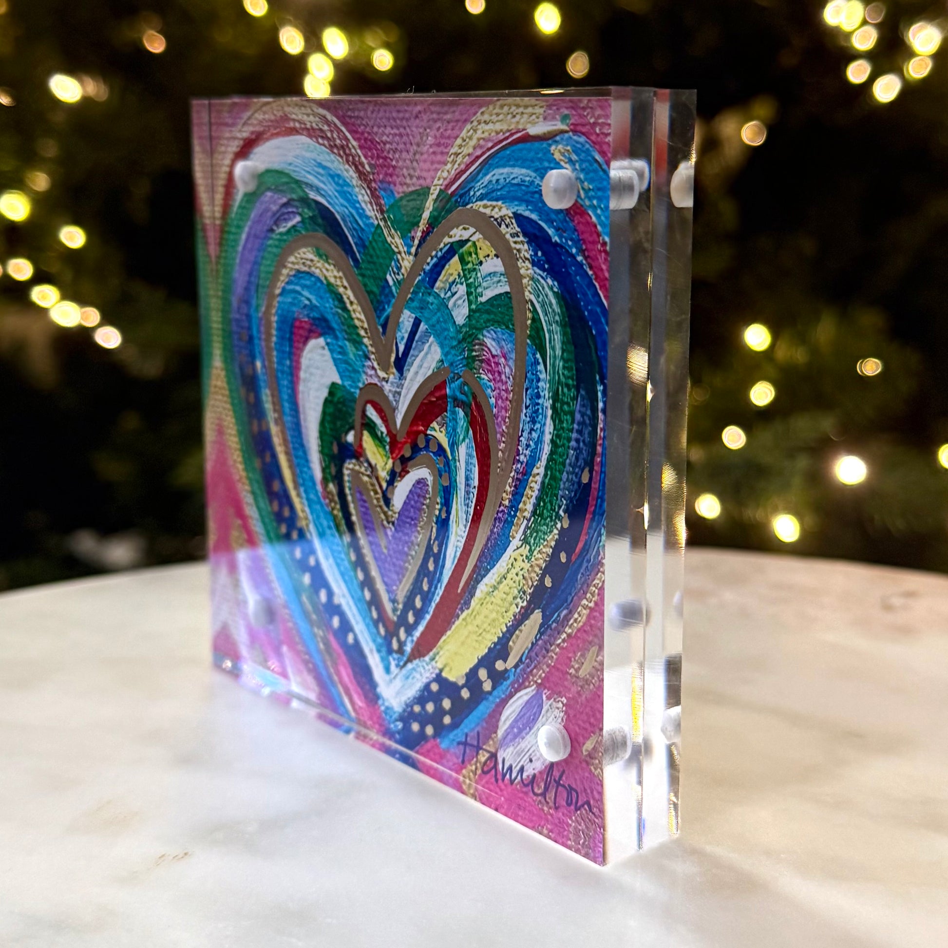 Colorful heart-shaped artwork on a clear block with blurred lights in the background