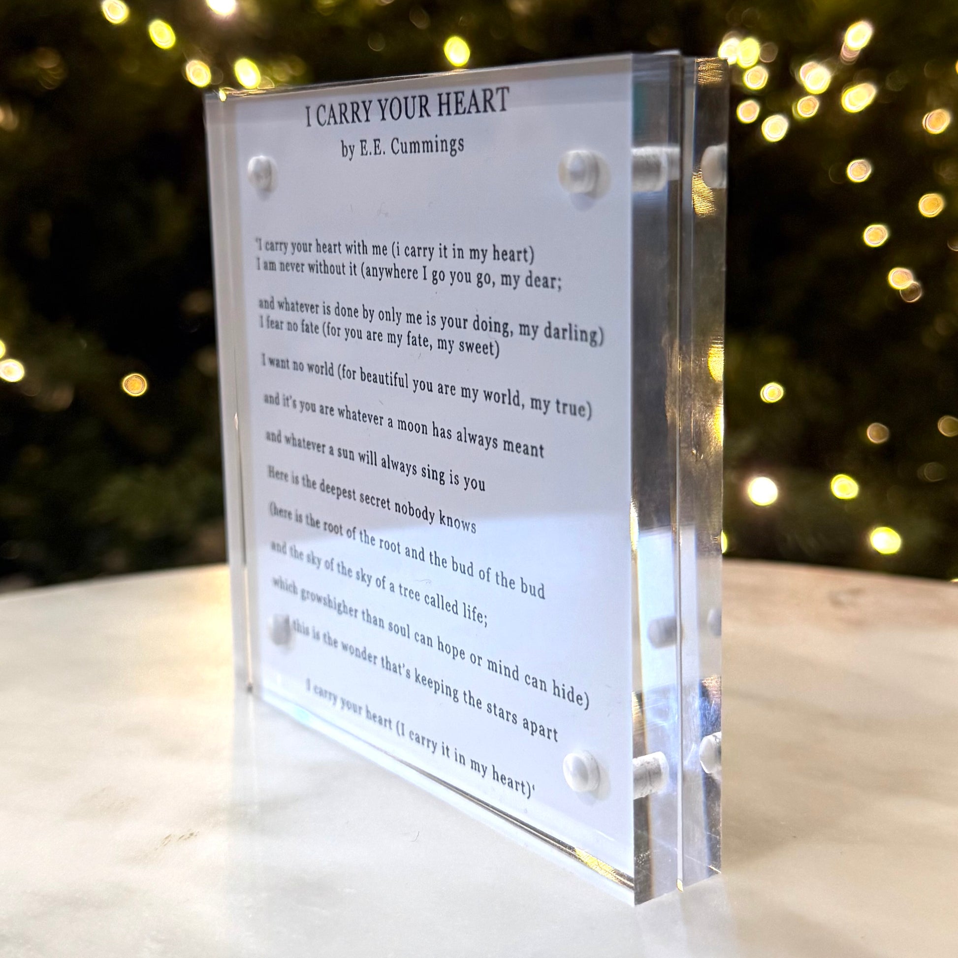Acrylic block with poem 'I Carry Your Heart' by E.E. Cummings against a blurred light background