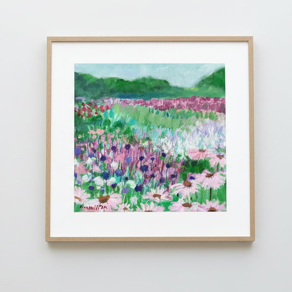 Framed artwork of a colorful floral landscape with mountains on a white wall.