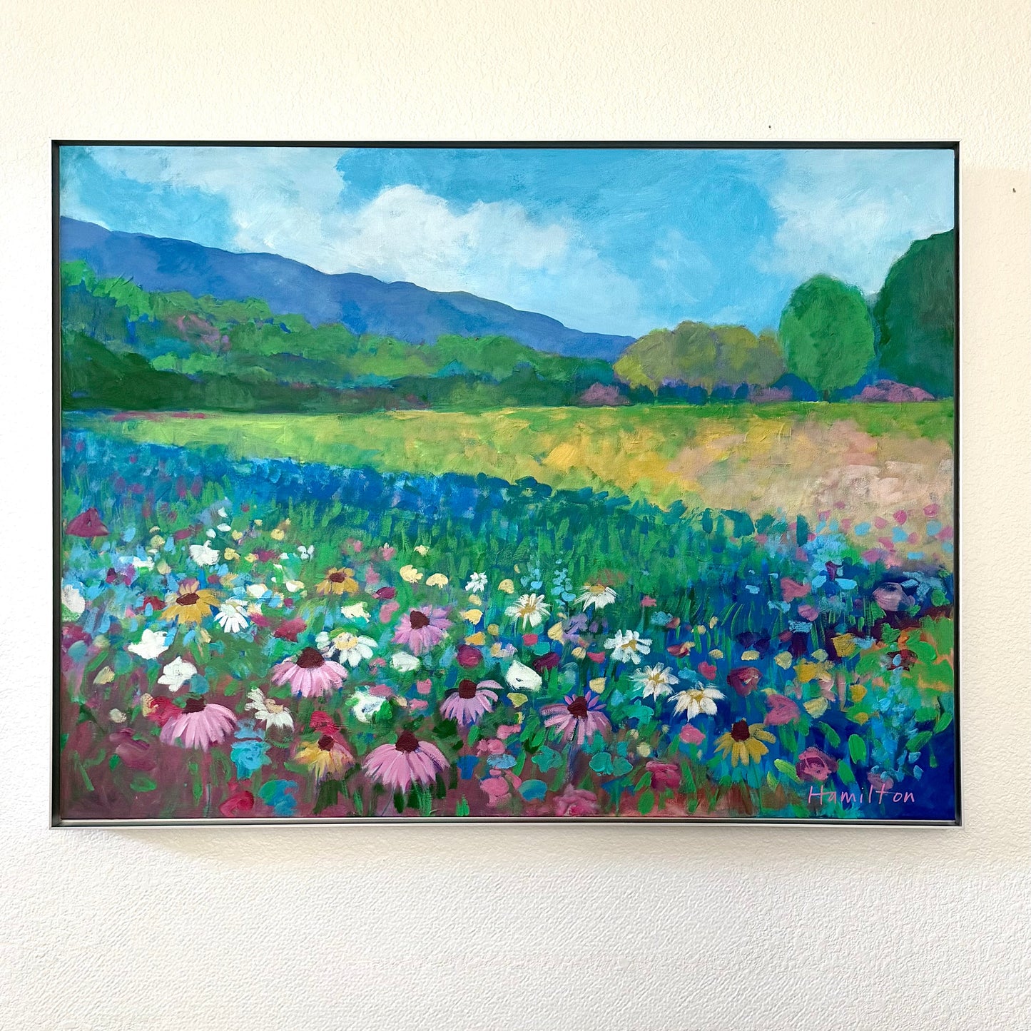 A large acrylic floral landscape by phoenix artist julie hamilton in shades of pink blue, white, green on a white wall.