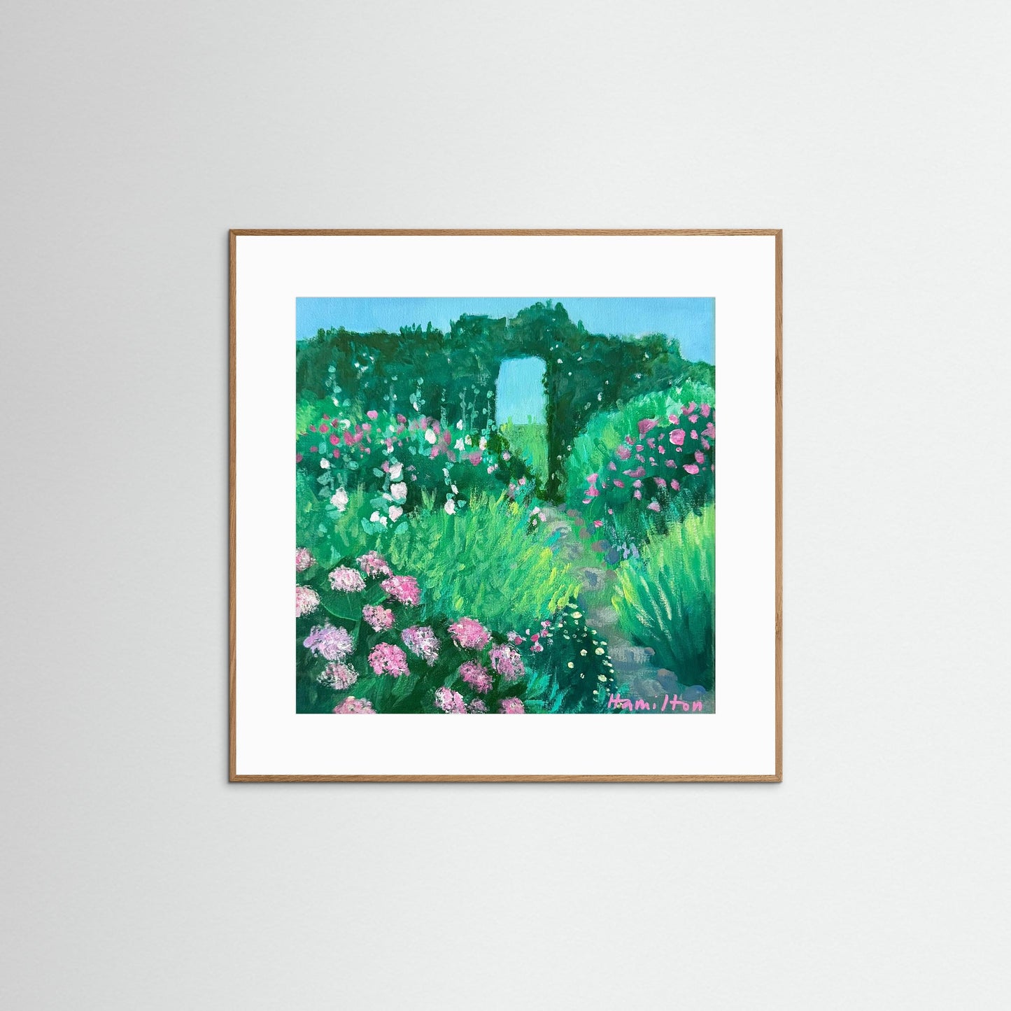 Framed artwork of a garden scene with flowers and a pathway on a white wall.